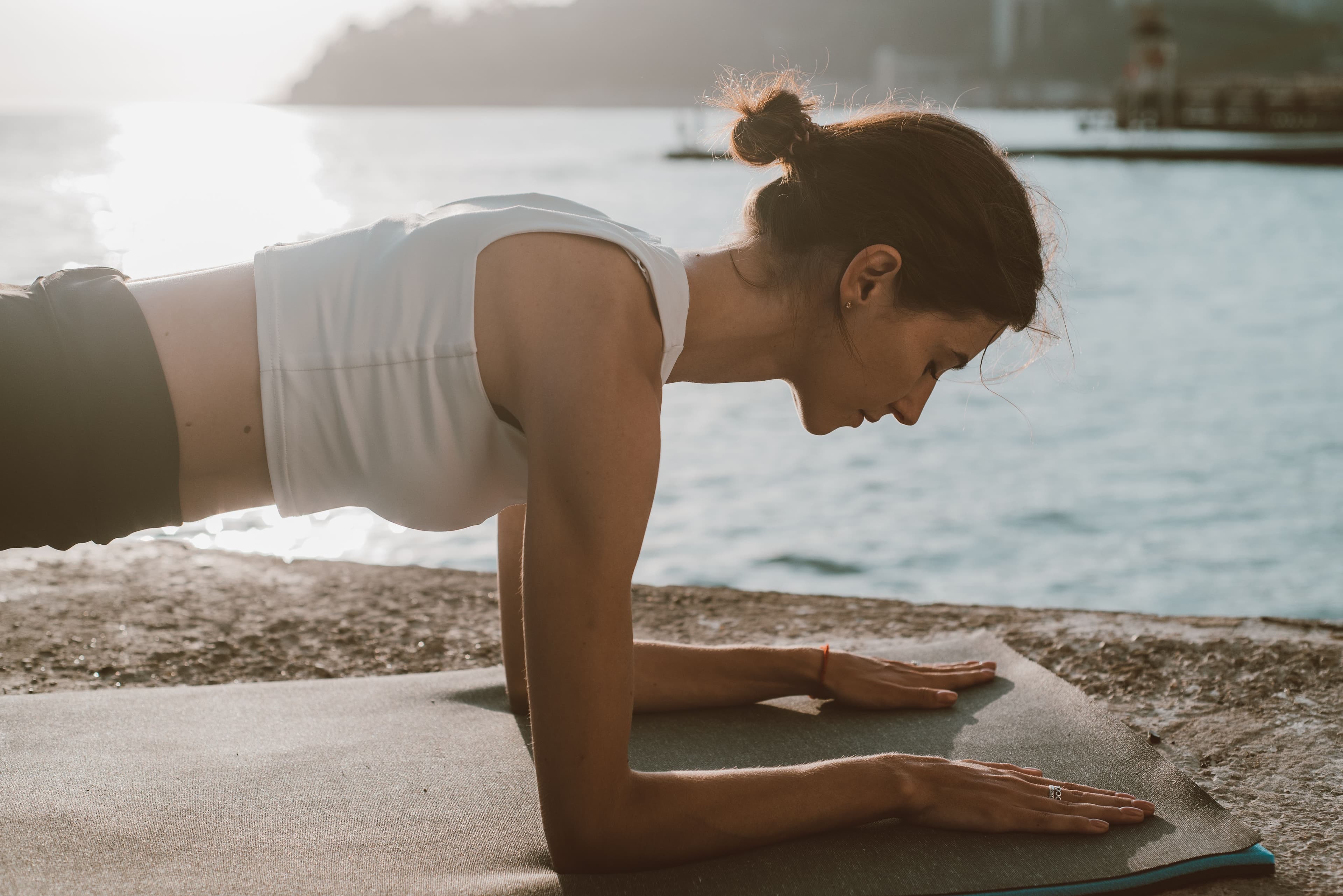 A woman holding a plank on an exercise mat by the water, representing a simple beginner strength routine