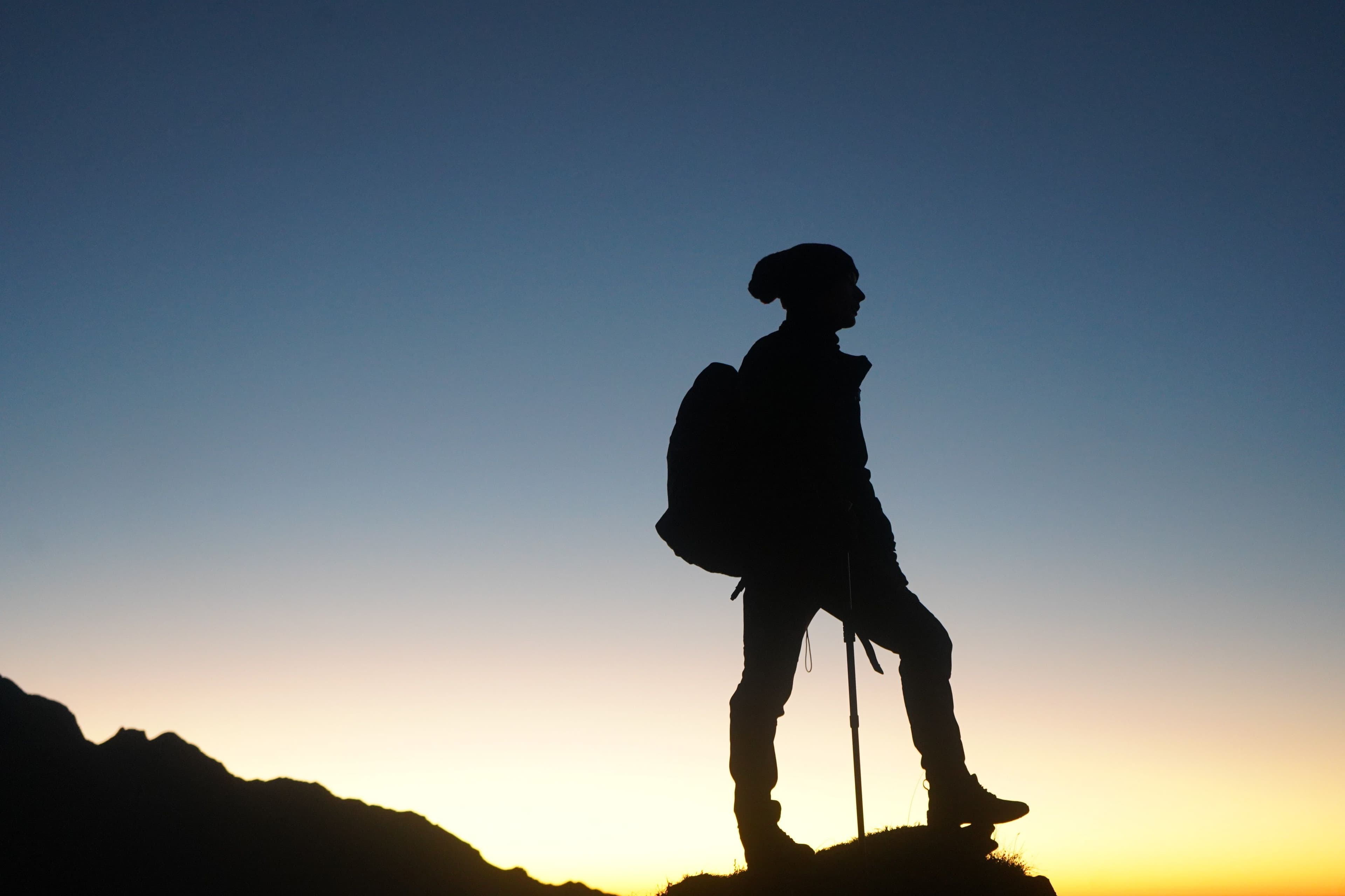 A silhouetted hiker standing on a mountain ridge at sunrise, representing beginner mountain hiking and outdoor cardio
