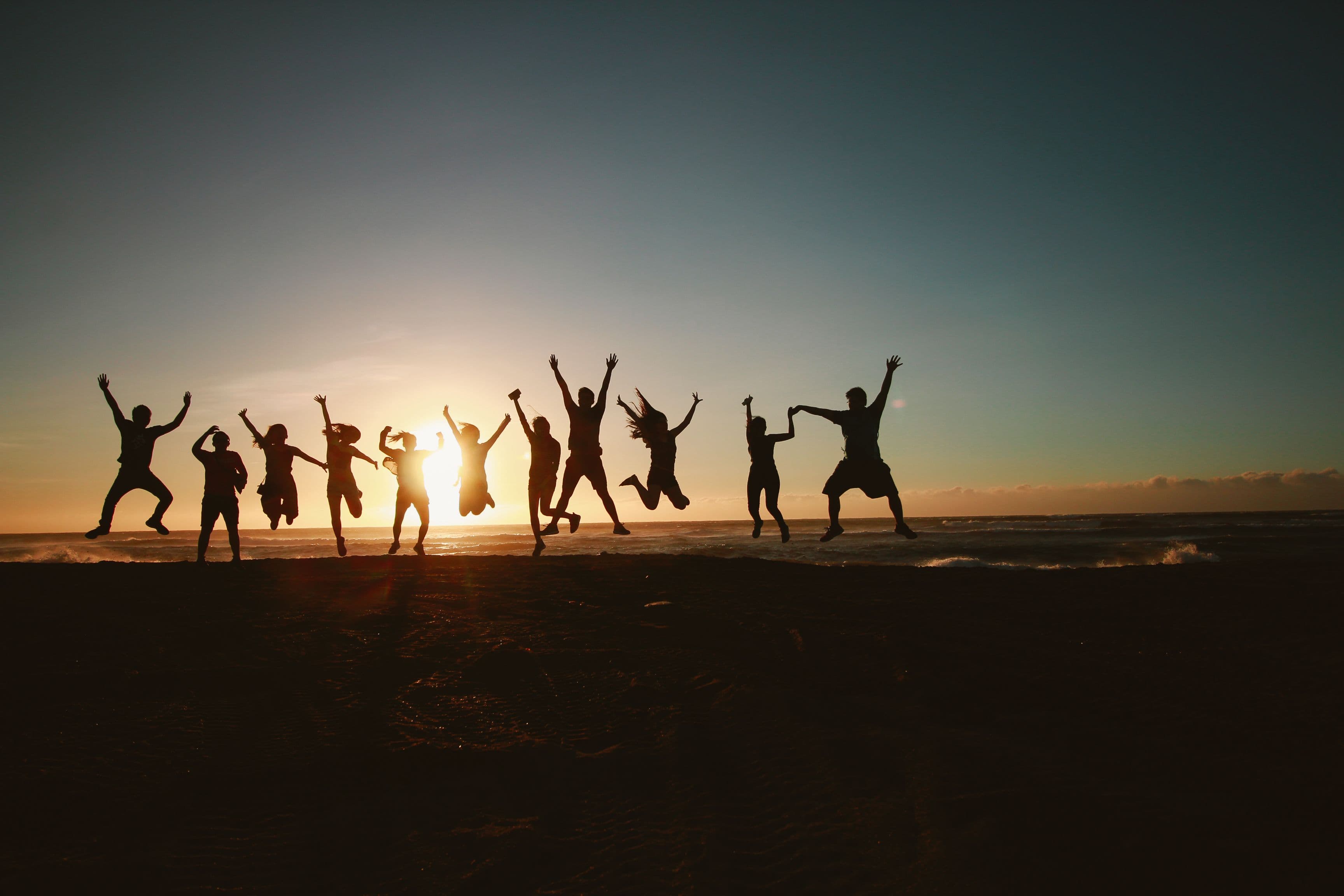 A group of people jumping on a beach at sunset