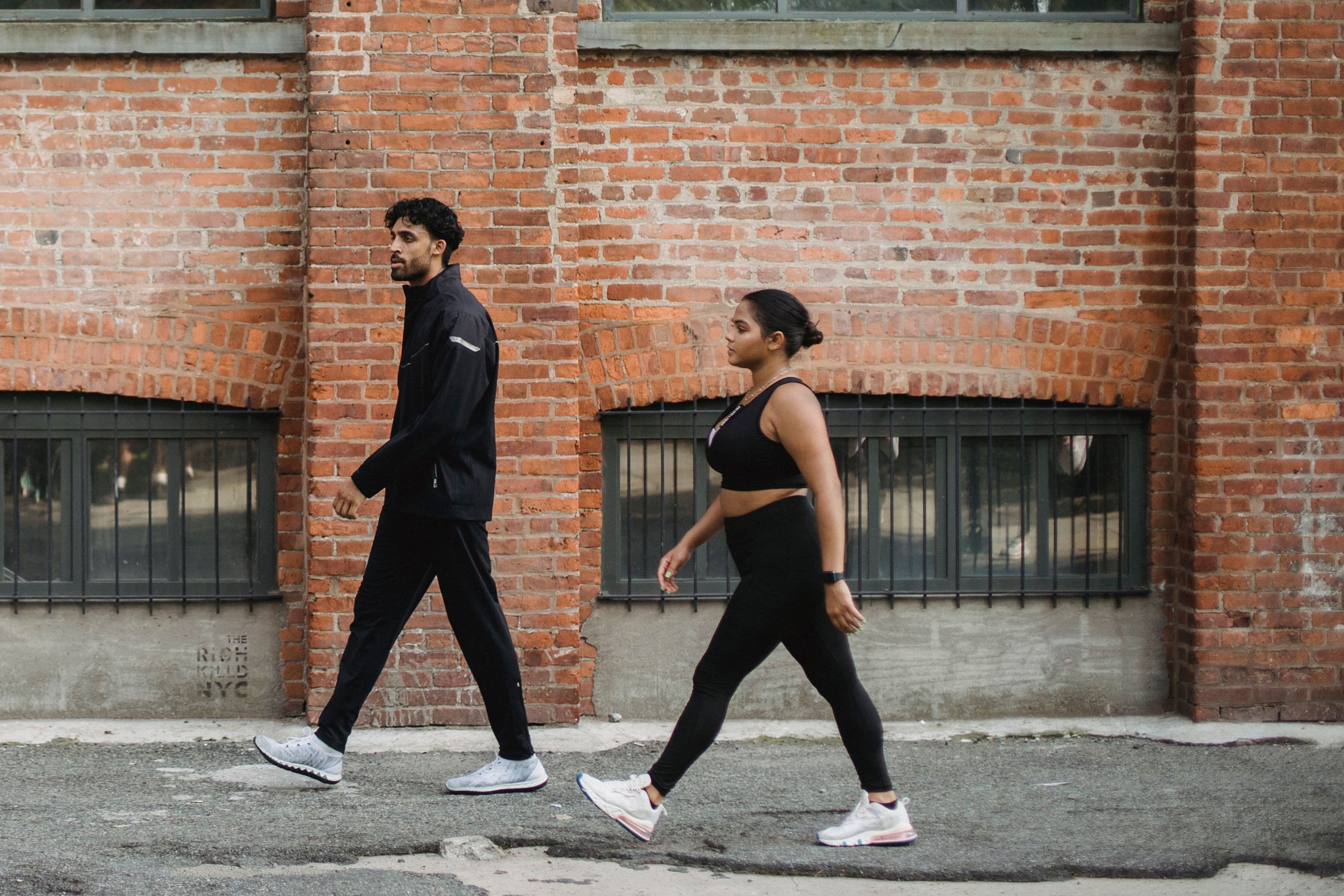 Two people walking outdoors beside a brick building